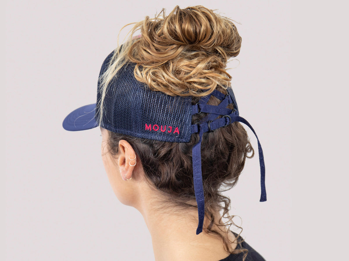 Ponytail baseball hat with blue and pink print. Mesh trucker style. Rear opening with cross tie. Model wearing a ponytail cap.