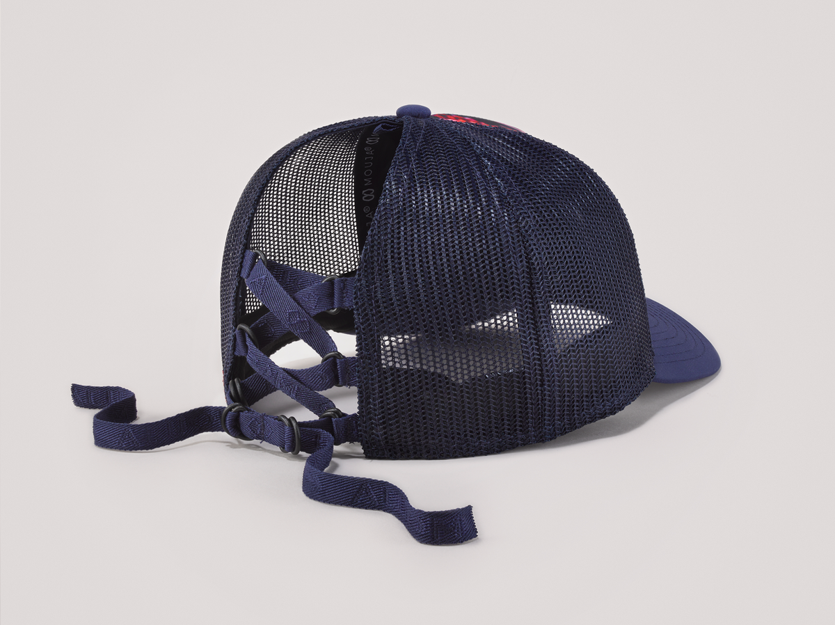 Ponytail baseball hat with blue and pink print. Mesh trucker style. Rear opening with cross tie. Oblique view.
